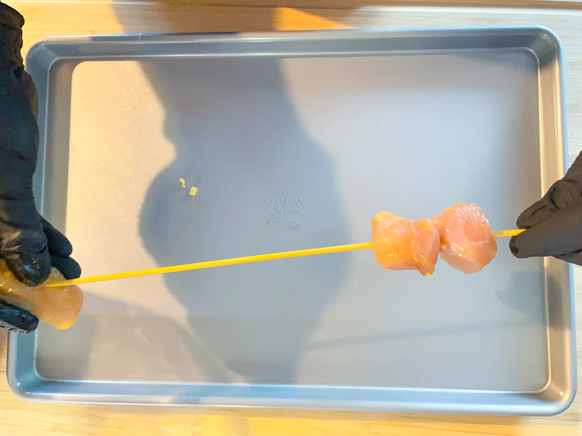 Chicken being threaded onto a bamboo skewer