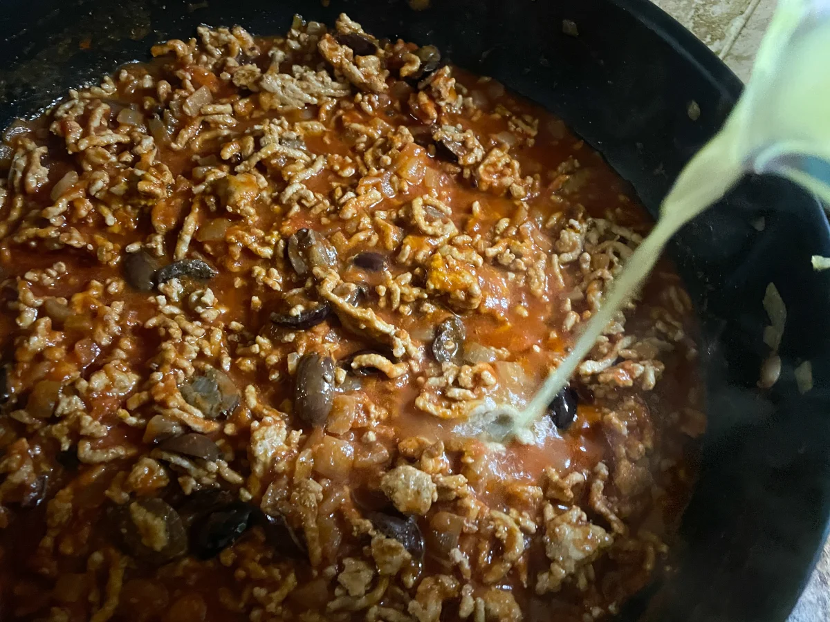 Chicken stock being poured into a pan of pork and tomato sauce