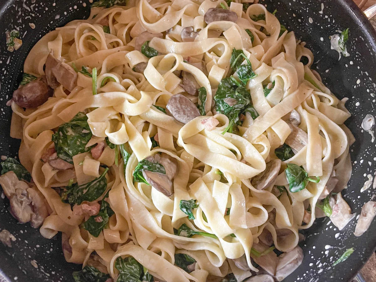 Fettuccine added to the pan coated in a creamy sauce
