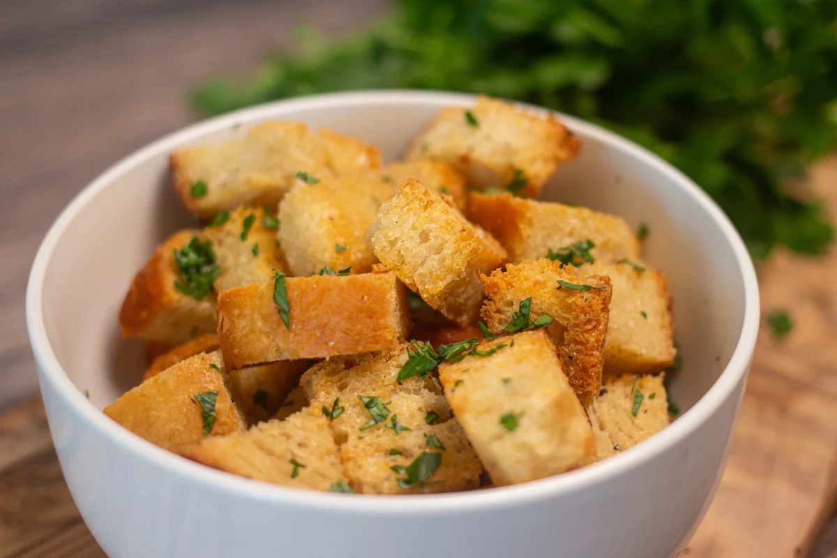 Homemade chunky croutons piled in a bowl with some parsley in the background