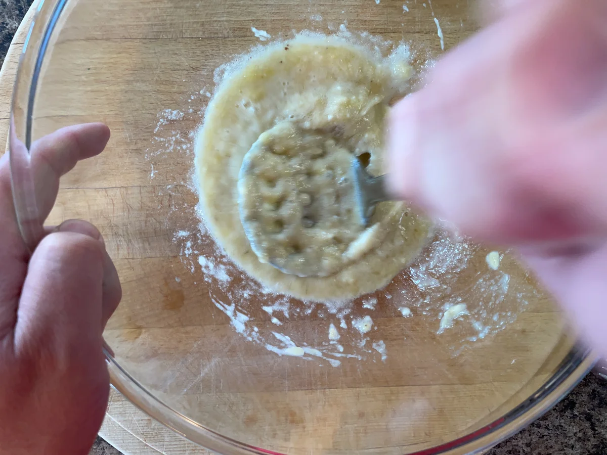 Mashing bananas in a large mixing bowl