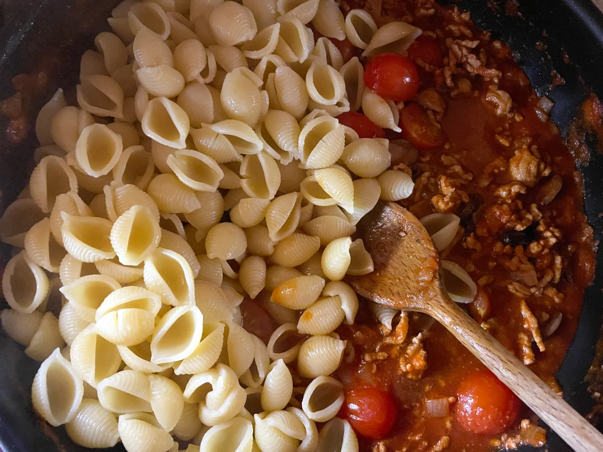 Shell pasta added to a pan of spicy pork and tomato sauce
