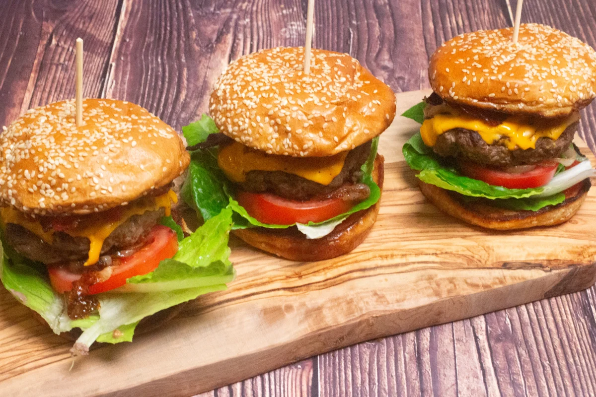 Three bacon cheese burgers on a wooden board
